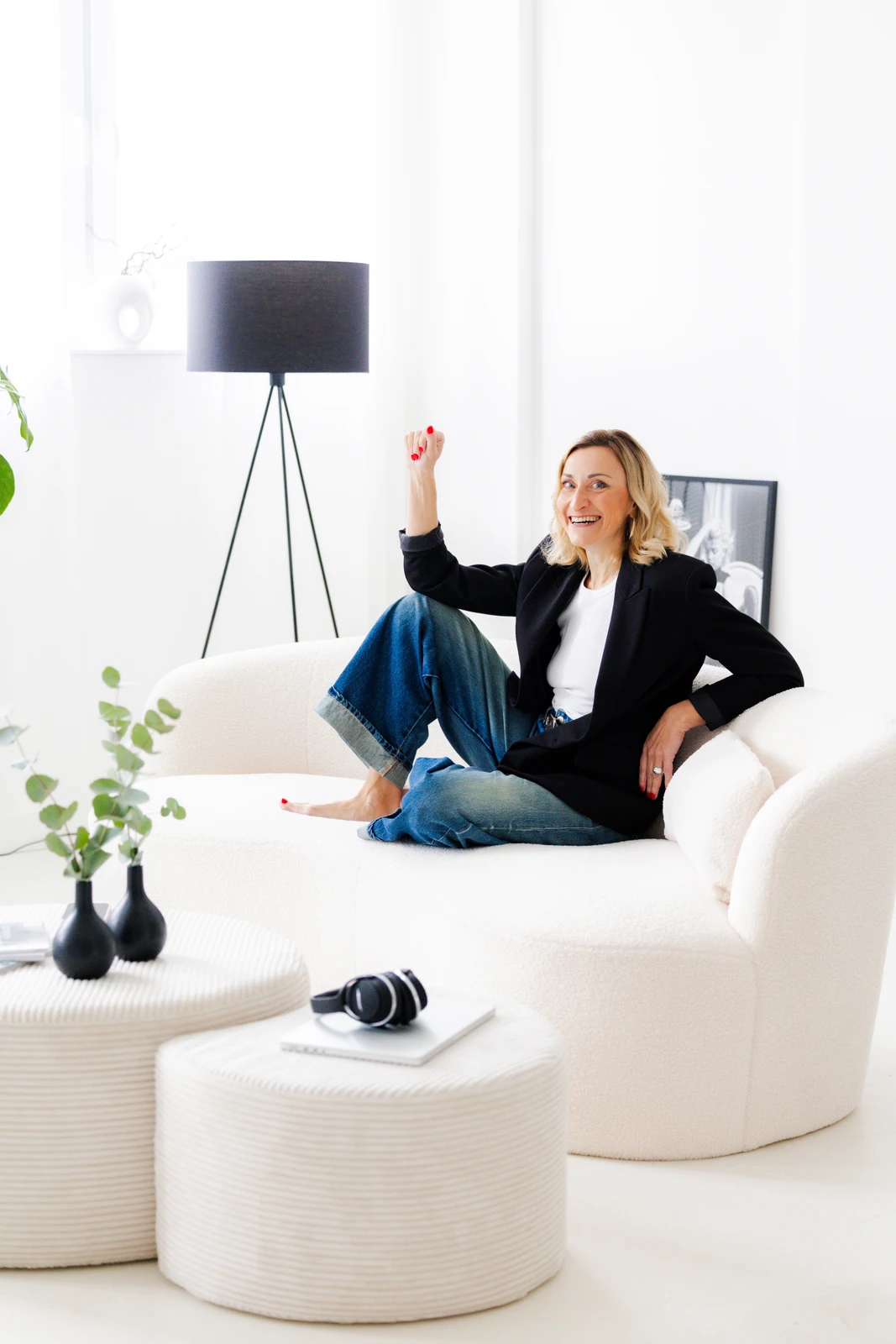 Jacqueline Schürer auf hellem Sofa Jacqueline Schürer im schwarzen Blazer und Jeans auf einem cremefarbenen Sofa mit einer angehobenen Hand