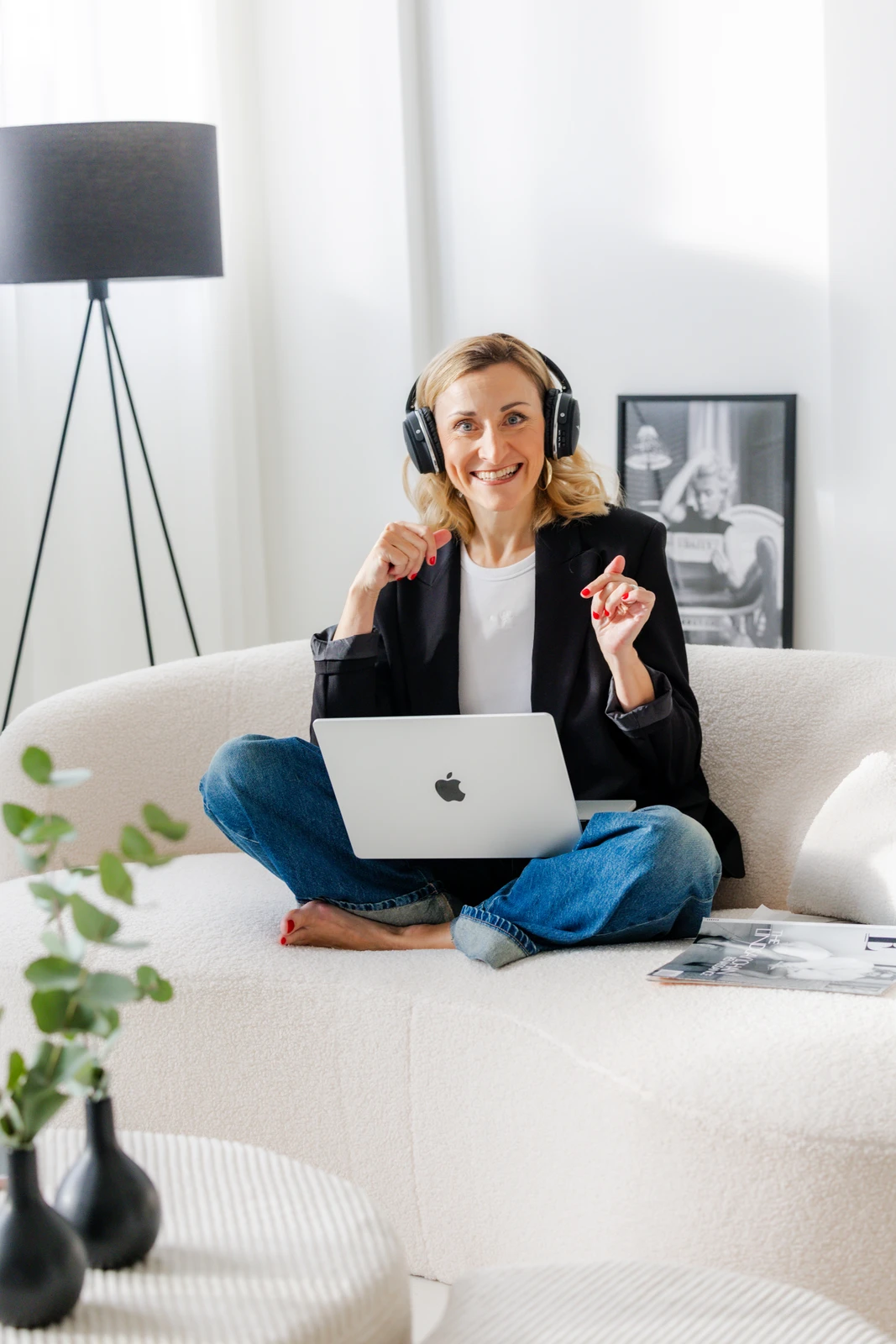 Unternehmerin mit Kopfhörern am Laptop Jacqueline Schürer arbeitet mit Kopfhörern und Laptop auf einem cremefarbenen Sofa