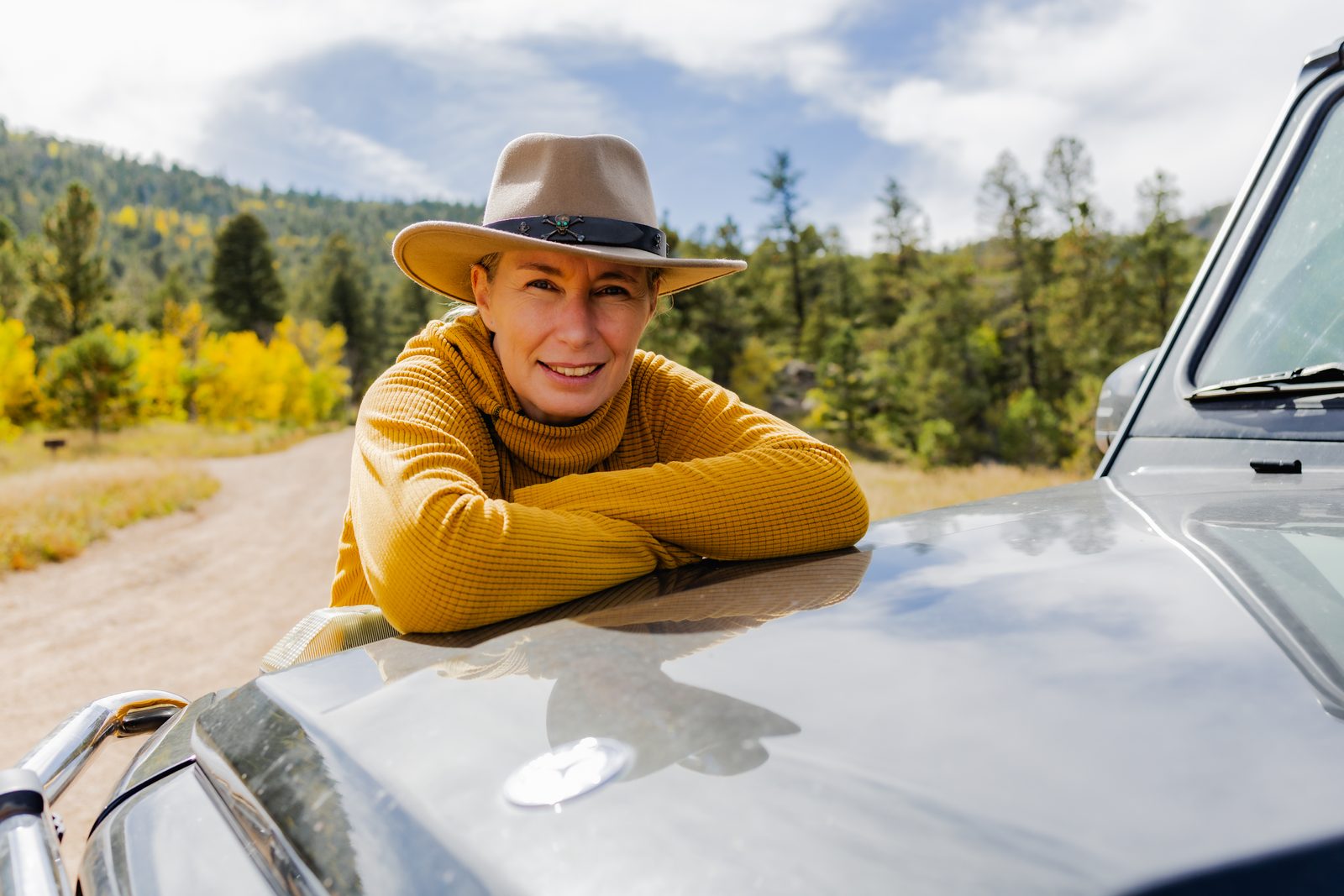 Unternehmerin mit Hut am Auto Eine Frau mit Hut und gelbem Pullover an einem Auto