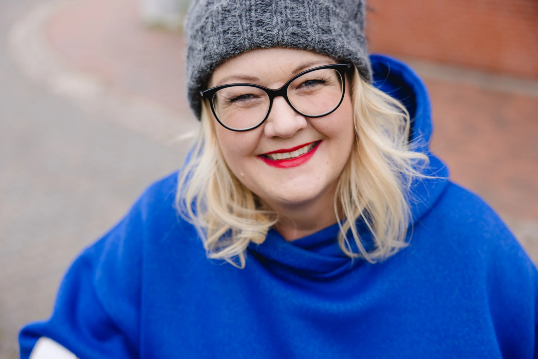 Lächelnde Unternehmerin mit Brille, grauer Mütze und blauem Schal im Businessportrait