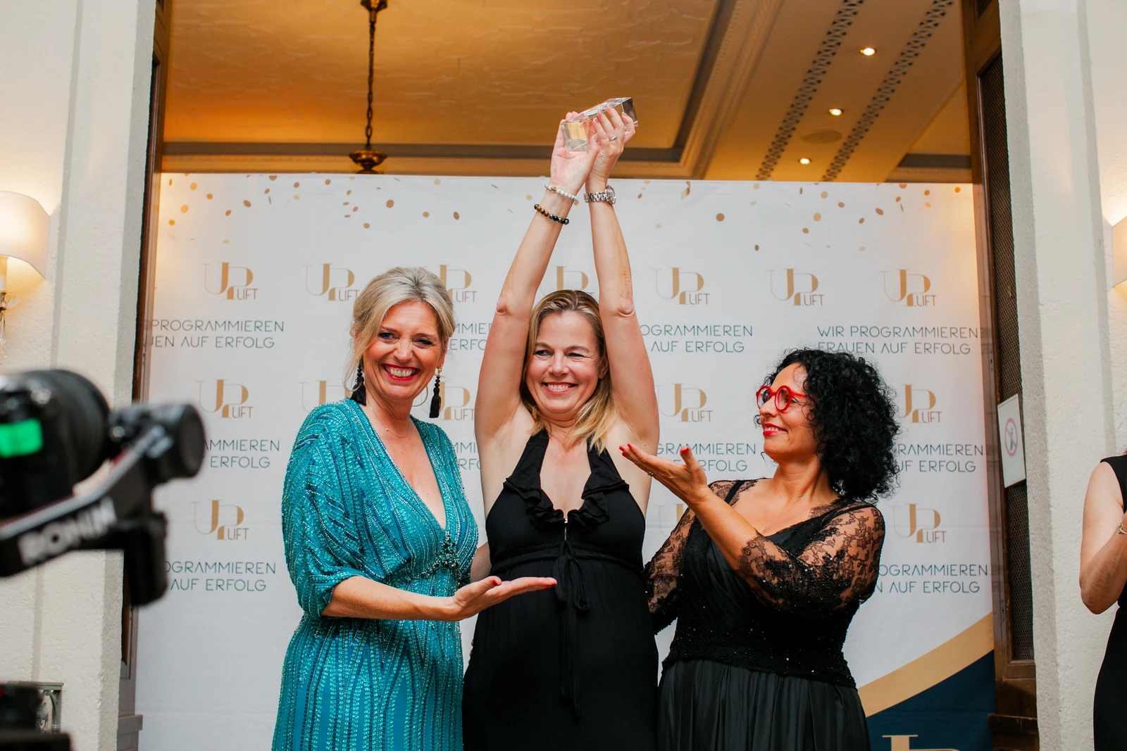 Auszeichnung in Heidelberg Drei Frauen lächeln bei einem UP-Lift Event in Heidelberg vor der Veranstaltungswand; eine hält eine Auszeichnung hoch