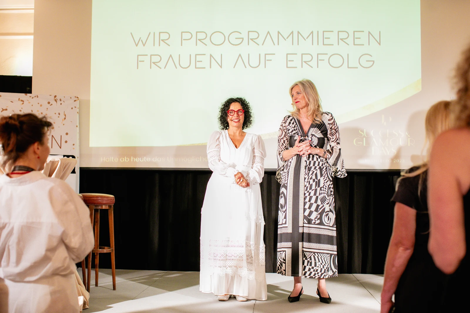 Zwei Frauen auf der Bühne Zwei Frauen stehen bei einem UP-Lift Event in Heidelberg vor der Projektion Wir programmieren Frauen auf Erfolg auf der Bühne