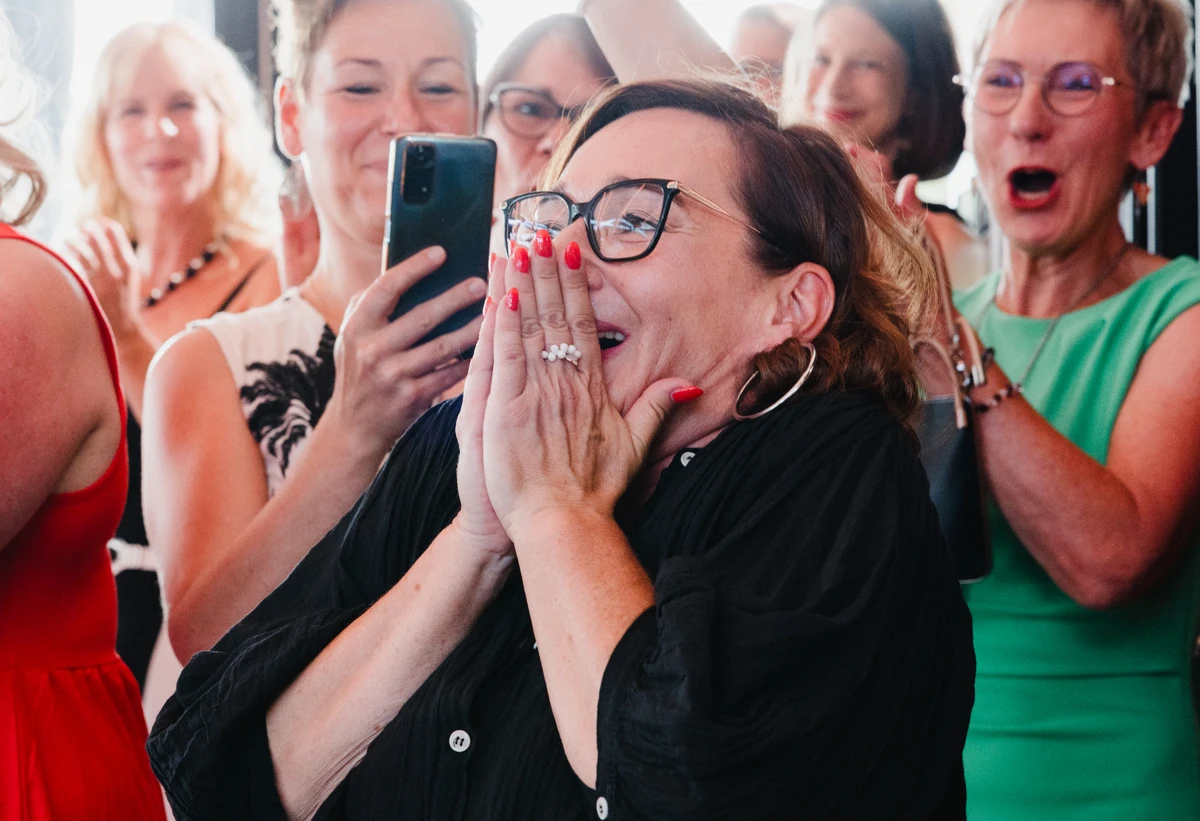 Frau mit Brille hält die Hände vor ihr Gesicht, umgeben von anderen Frauen bei einer Veranstaltung