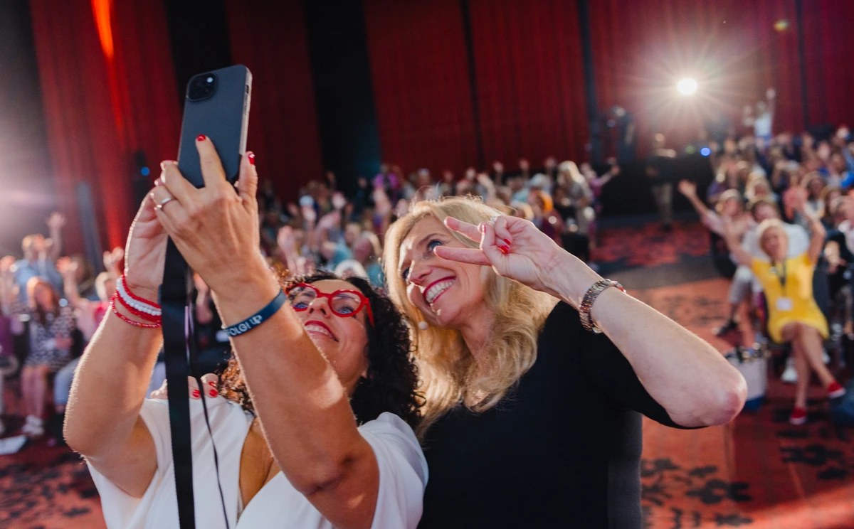 Zwei Frauen machen ein Selfie vor dem Publikum einer Veranstaltung