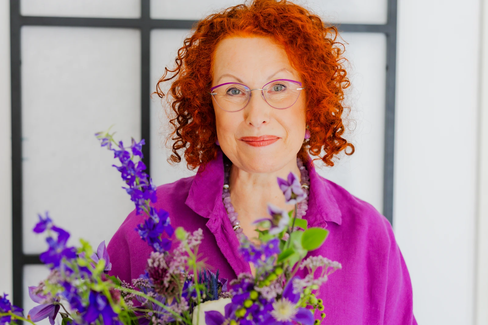 Hannah Wolter steht in lila Bluse hinter einem Blumenstrauß im Studio in Hannover. Fotografie: Manuela Engelking.
