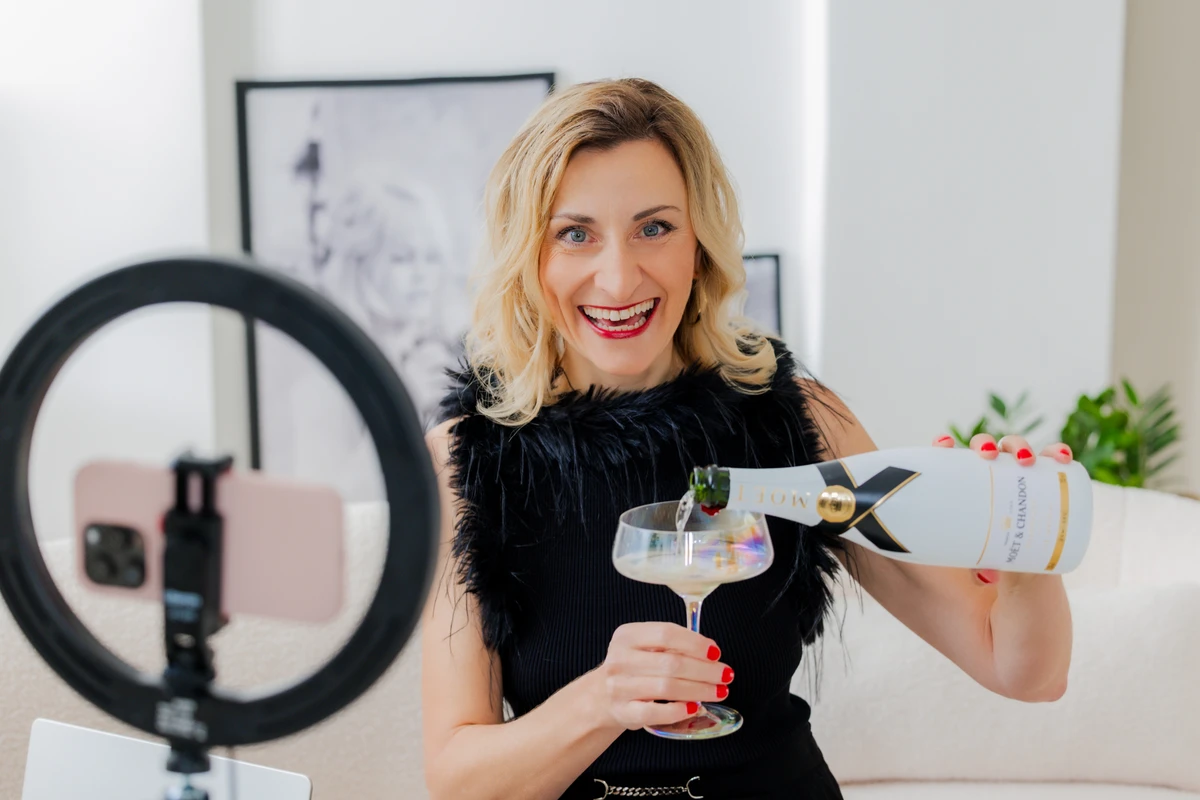 Coachin gießt Sekt vor einer Ringlampe ins Glas. Fotografin: Manuela Engelking. Aufnahmeort: Hamburg im Studio.