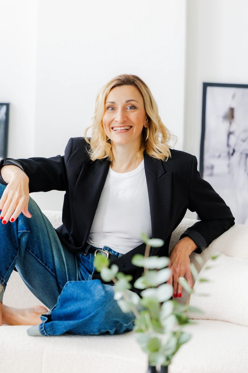 Coachin sitzt lachend im Blazer auf einem Sofa. Fotografin: Manuela Engelking. Aufnahmeort: Hamburg im Studio.