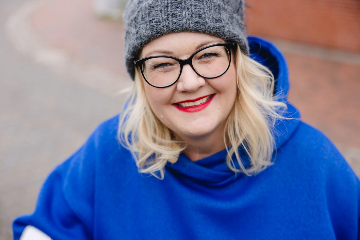 Unternehmerin mit Brille und Strickmütze lächelt. Fotografin: Manuela Engelking. Aufnahmeort: Flensburg.