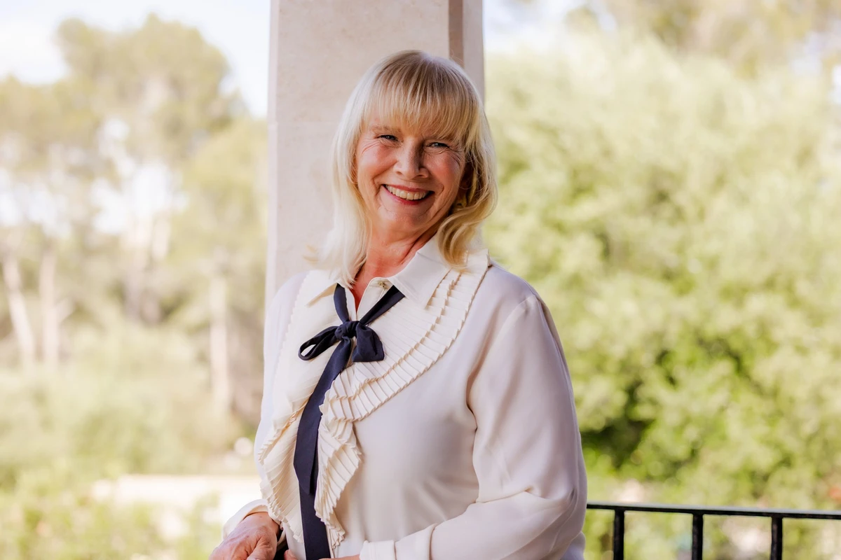 Unternehmerin lächelt in weißer Bluse auf einer Terrasse. Fotografin: Manuela Engelking. Aufnahmeort: Mallorca.