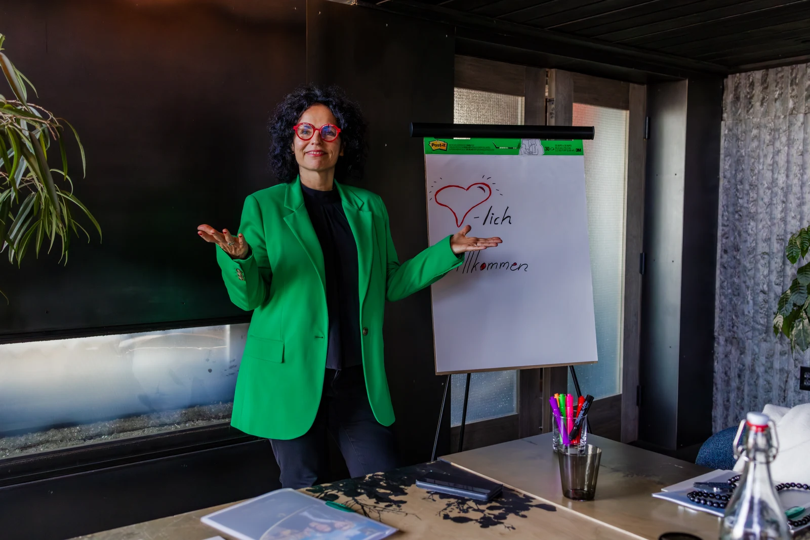Arbeit am Flipchart Frau mit grüner Jacke und roter Brille steht neben einem Flipchart
