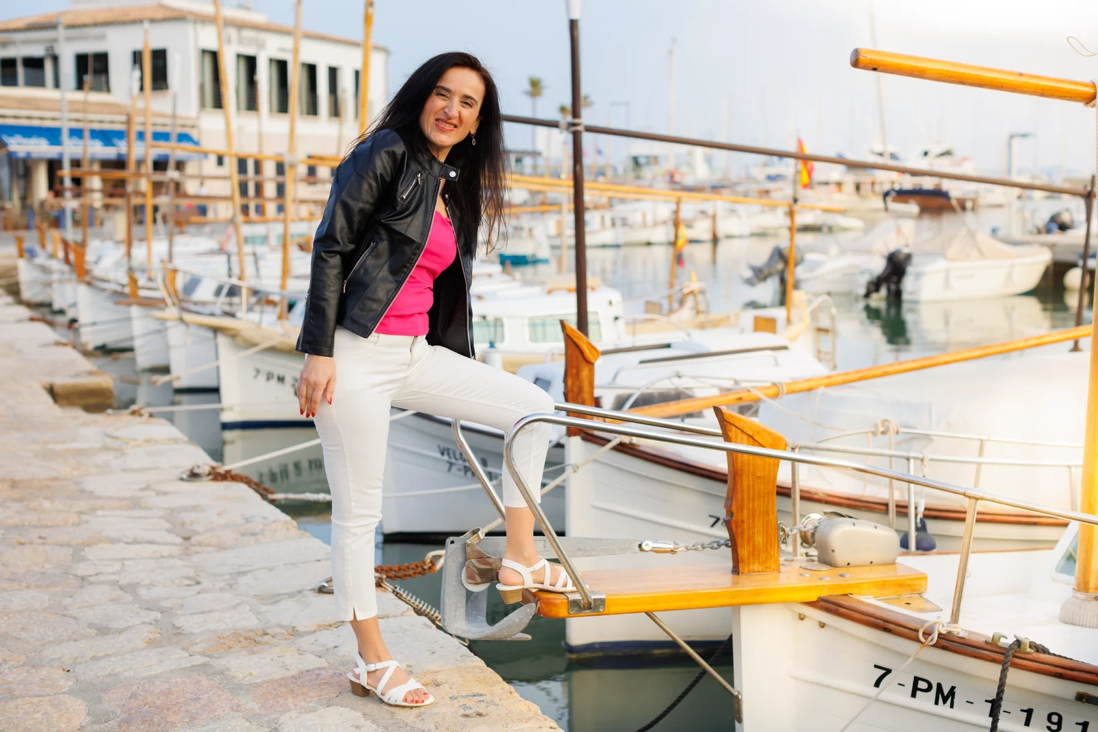 Unternehmensfotografie auf Mallorca: Frau in schwarzer Jacke und weißer Hose steht an einem Boot im Hafen.